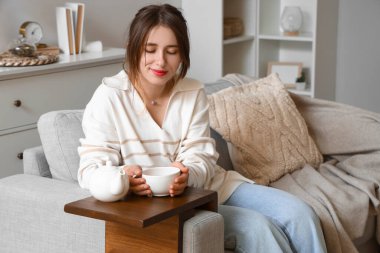 Evde bir fincan sıcak çayla genç bir kadın.