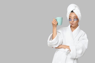 Göz altı bantları ve arka planda kahve fincanı olan düşünceli Asyalı genç bir kadın.