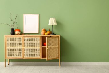 Balkabaklı ahşap dolap, lamba ve yeşil duvarın yanındaki boş çerçeve.