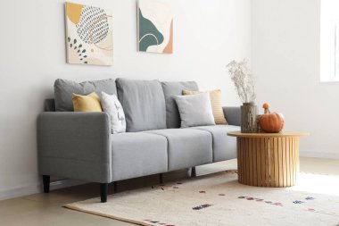 Oturma odasının içi. Gri kanepe, çiçekler ve ahşap sehpada balkabağı.