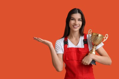 Altın bardaklı kadın işçi turuncu arka planda bir şey gösteriyor.