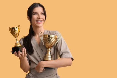 Sarı arka planda altın bardakları olan genç bir kozmetolog.