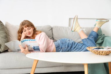 Evdeki kanepede dergi okuyan genç bir kadın.