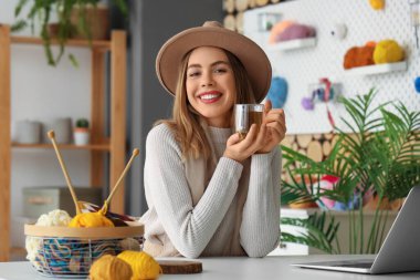 Evde çay içip örgü ören genç bir kadın var.