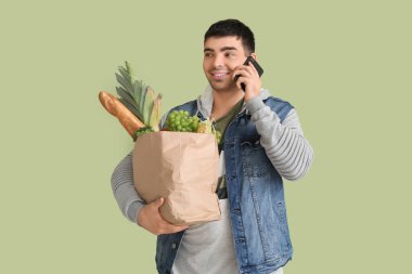 Bakkal çantalı genç adam yeşil arka planda cep telefonuyla konuşuyor.