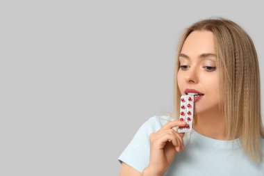 Young woman with blister of vitamin A pills on light background clipart