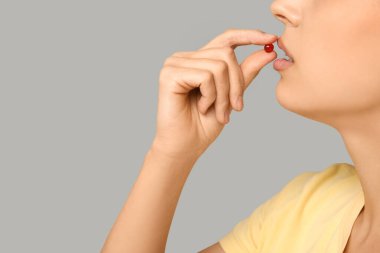 Gri arka planda A vitamini kapsülü alan güzel genç kadın, yakın plan.