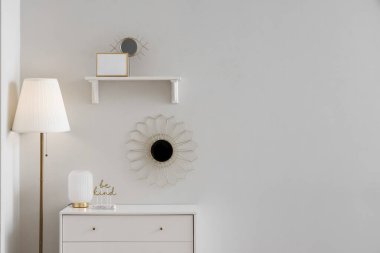 Beyaz duvarın yanında lamba, ayna ve dekor olan çekmeceler.