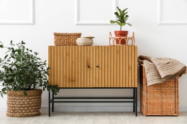 Beyaz duvarın yanında saksıları ve hasır sepetleri olan tahta bir dolap.