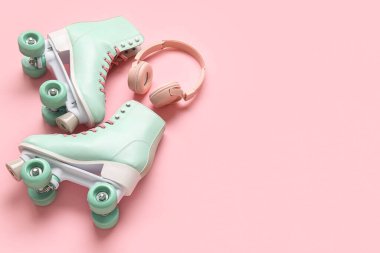 Pembe arka planda bir çift eski paten ve modern kulaklık.