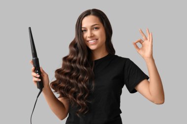 Saç maşası olan güzel bir kadın gri arka planda iyi görünüyor.