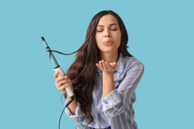 Mavi arka planda saç maşasıyla öpüşen güzel genç bir kadın.