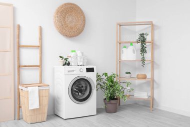 Sepeti, raf ünitesi ve beyaz duvarın yanındaki merdiveni olan modern çamaşır makinesi. Ev çamaşır odasının içi.