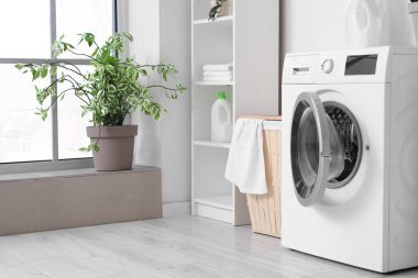 Beyaz duvarın yanında sepet ve raf ünitesi olan modern çamaşır makinesi. Ev çamaşır odasının içi.