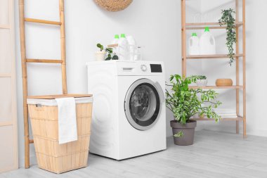 Sepeti, raf ünitesi ve beyaz duvarın yanındaki merdiveni olan modern çamaşır makinesi. Ev çamaşır odasının içi.