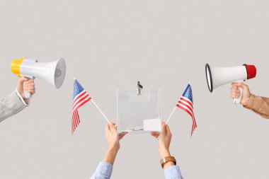 Eller oy sandığını tutuyor, beyaz arka planda Amerikan bayrakları ve megafonları var. Seçim kavramı