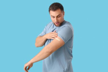 Mavi arka planda uygulamalı tıbbi yaması olan genç bir adam. Aşılama kavramı