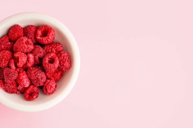 Pembe arka planda dondurulmuş ahududulu bir kase.