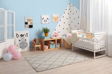 Çocuk odasındaki renkli duvarın yanında oyuncak ve bebek beşiği olan raf ünitesi.