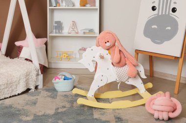 Oyuncak tavşan sallanan atın üstünde, çocuk odasının içinde, yakın plan.