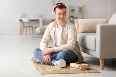 Genç adam sesli kitabı dinliyor ve oturma odasındaki kanepenin yanında oturuyor.