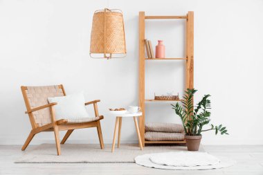 Beyaz oturma odasının içinde rahat koltuk, saksı ve raf ünitesi var.