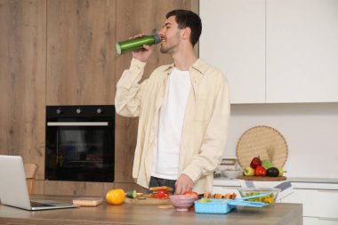 Mutfakta beslenme çantası hazırlarken su içen genç bir adam.