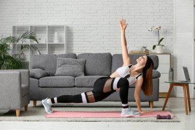 Güzel genç bir kadın oturma odasında yoga yapıyor.