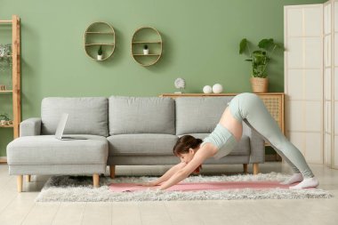 Güzel genç bir kadın oturma odasında yoga yapıyor.