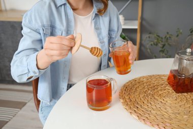 Genç bir kadın mutfaktaki çaya bal ekliyor.