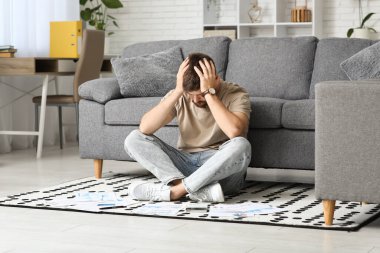 Stresli, borç içindeki genç adam evde yerde oturuyor.