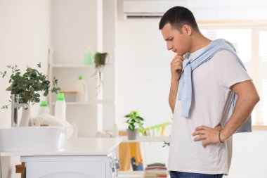 Çamaşır odasındaki çamaşır makinesinin yanında düşünceli bir genç adam.