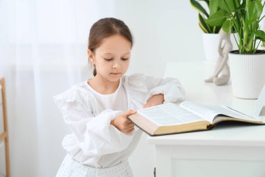 Evdeki çekmecelerin üstünde İncil okuyan tatlı küçük kız.
