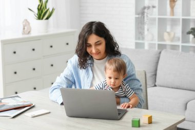 Sevimli bebek ve evde doğum izninde dizüstü bilgisayarla çalışan mutlu genç anne.