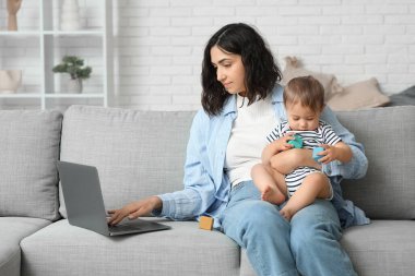Evde doğum izninde dizüstü bilgisayarla çalışan tatlı bebek ve genç anne.