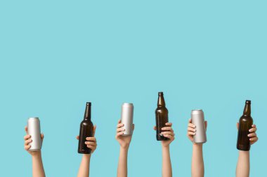 Şişelerde taze bira ve mavi arka planda teneke kutu olan kadın elleri.