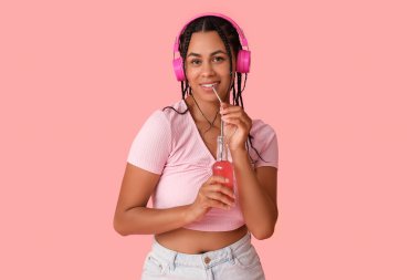 Limonatalı genç Afro-Amerikalı kadın pembe arka planda müzik dinliyor.