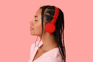 Genç Afro-Amerikalı kadın pembe arka planda müzik dinliyor.
