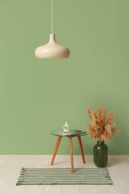 Asılı lamba, otlaklar ve yeşil duvarın yanındaki insan figürlü kahve masası ve şarjör.
