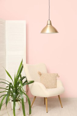 Sallanan lamba, koltuk, katlanan ekran ve pembe duvarın yanındaki çiçek.