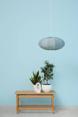 Asılan lamba ve bankta mavi duvarın yanında çiçekler var.