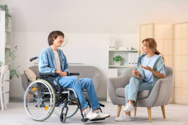 Kadın psikolog, ofiste tekerlekli sandalyedeki çocukla konuşuyor.