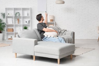 Yakışıklı genç adam oturma odasında klimayı açıyor.