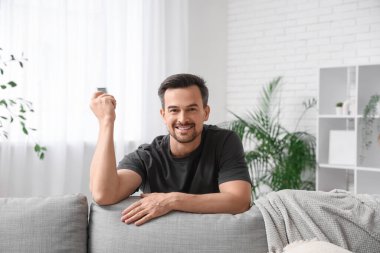 Yakışıklı genç adam oturma odasında klimayı açıyor.