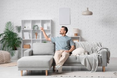 Yakışıklı delikanlı kanepede oturuyor ve oturma odasındaki klimayı açıyor.