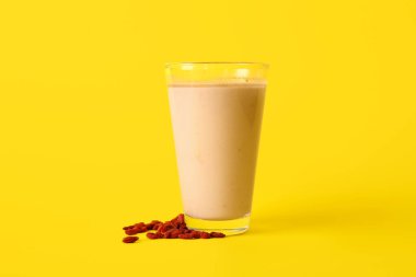 Sarı arka planda bir bardak taze goji meyveli smoothie.