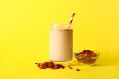 Bir bardak taze goji smoothie ve sarı arka planda böğürtlenli kase.