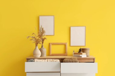 Kalın elbiseli çekmeceler, kitaplar, çiviler ve duvarda asılı boş resim çerçeveleri.