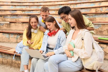 Dışarıdaki banklarda dizüstü bilgisayarla çalışan bir grup öğrenci.