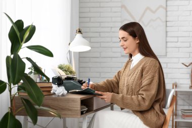 Güzel düşünceli kadın yazar. Daktiloyla odada, masada deftere yazıyor.